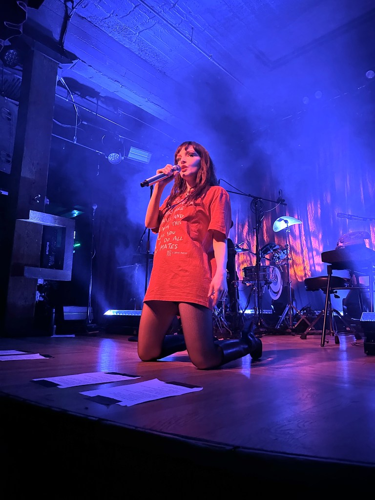 Lauren Mayberry kneels while singing 