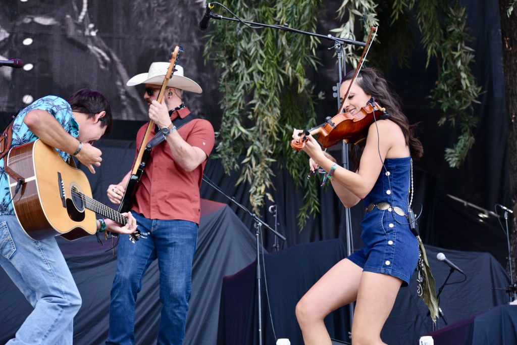 Wyatt Flores on guitar, Kenzie Sue Miracle playing fiddle, and Bill Peters on bass at Hinterland Music Festival 2025